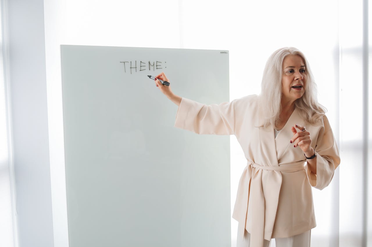 Adult female instructor teaching a theme on a whiteboard in a modern classroom setting.