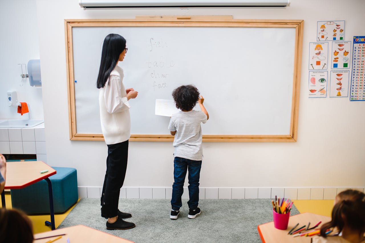 A teacher assists a young boy writing on a whiteboard in an engaging classroom setting.